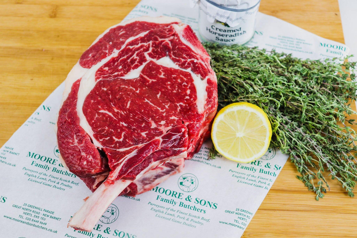 Rib Roast Cote de Beouf on a butcher block with lemon and herbs on the side