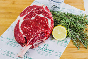 Rib Roast Cote de Beouf on a butcher block with lemon and herbs on the side