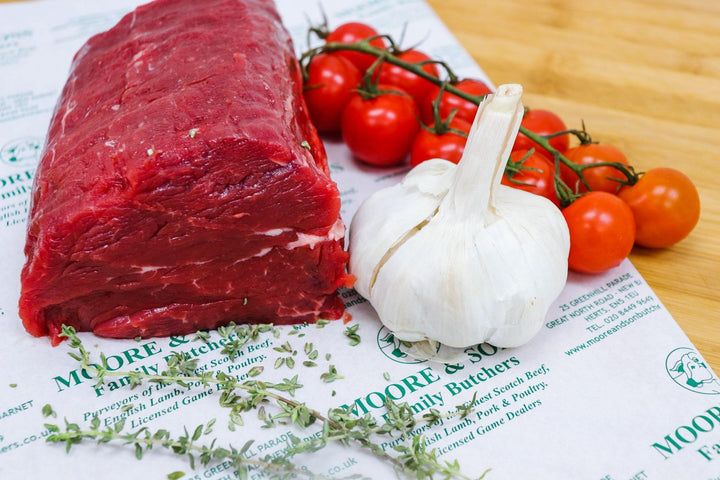 beef fillet cut on a butcher block next to tomatoes and garlic