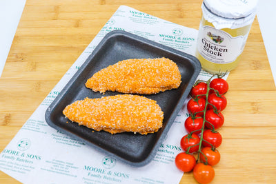 two pieces of chicken kiev on a butcher block, with tomatoes and chicken stock on the side