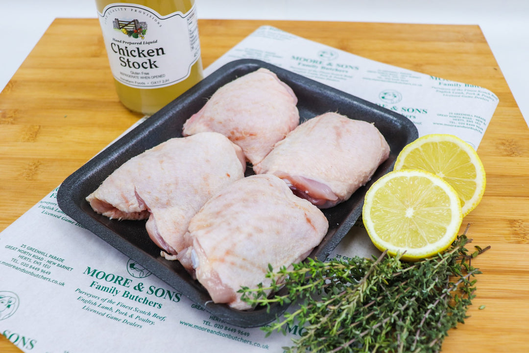 four chicken tights on a butcher block with lemon, herbs and chicken stock on the side