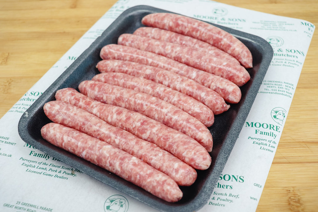 Ten chipolatas on a black tray on top of a butchers block