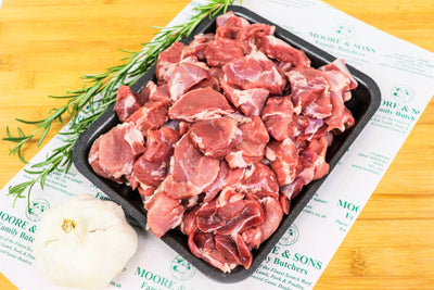 diced lamb on a butchers block with rosemary and garlic on the side