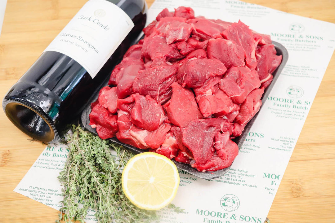 diced venison on a butchers block with lemon and herbs with a bottle of wine on the side