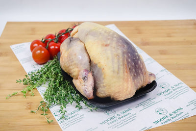 guinea fowl on a butchers block with tomatoes and herbs on the side
