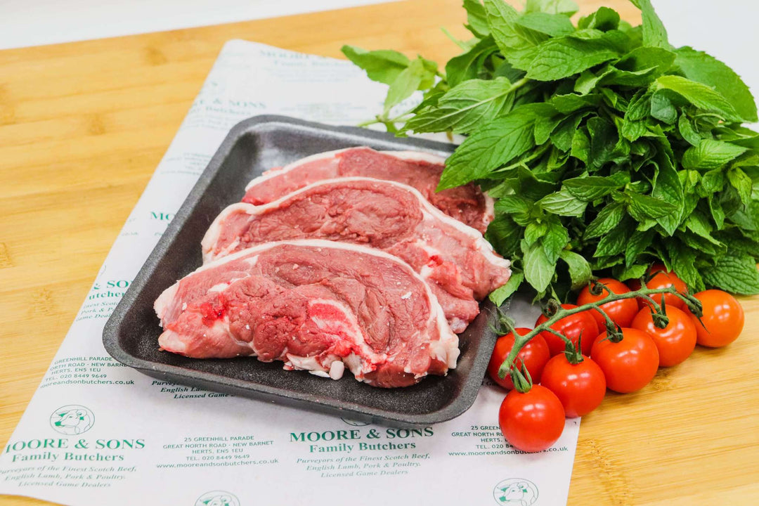 lamb chump chops on a butchers block with herbs and tomatoes on the side