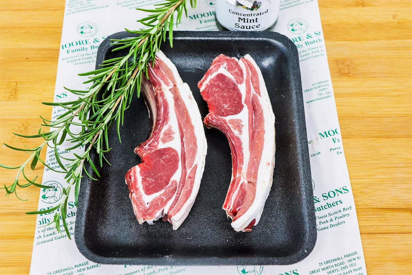 lamb cutlets on a tray with herbs and mint sauce on the side