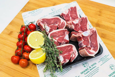 lamb loin chops on a butchers block with lemons and tomatoes on the side