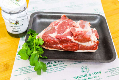 lamb rump on a tray with herbs and mint sauce on the side