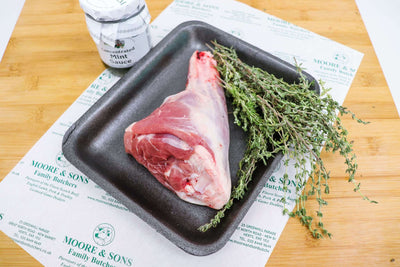 lamb shanks on a butchers block with herbs and mint sauce on the side