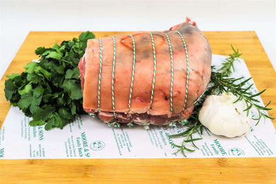 leg of lamb boneless rolled on a butchers block with herbs and garlic on the side