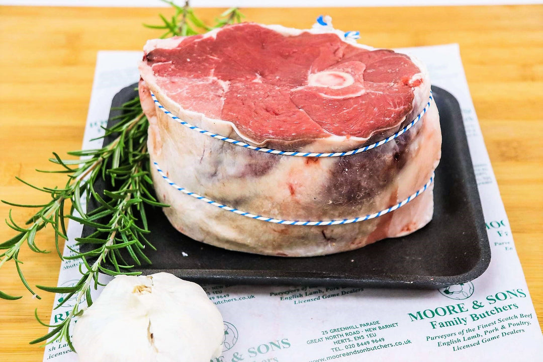 leg of lamg half fillet end on a butchers block with herbs and garlic on the side