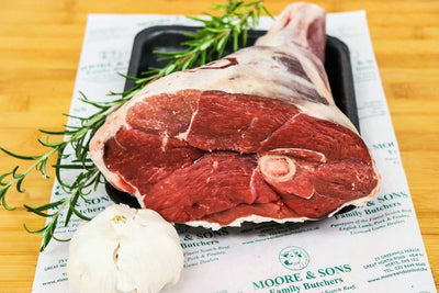 leg of lamb half knuckle end on a butchers block with herbs and garlic