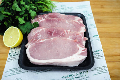 pork loin steaks on a butchers block with herbs and lemon on the side