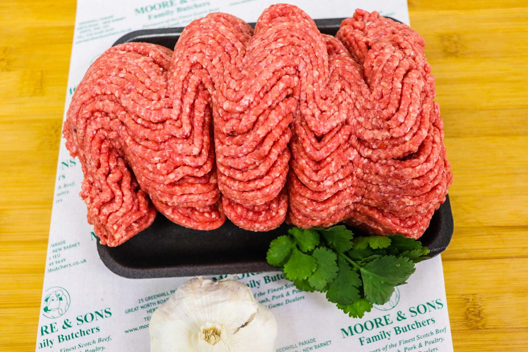 minced beef on a black tray with herbs and a garlic on the side