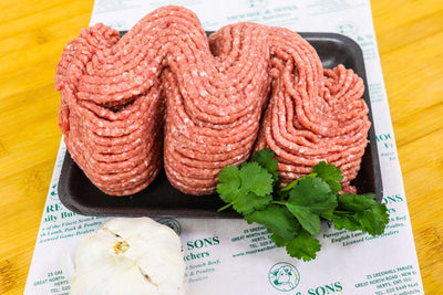 Minced lamb on a butchers block with herbs and garlic on the side