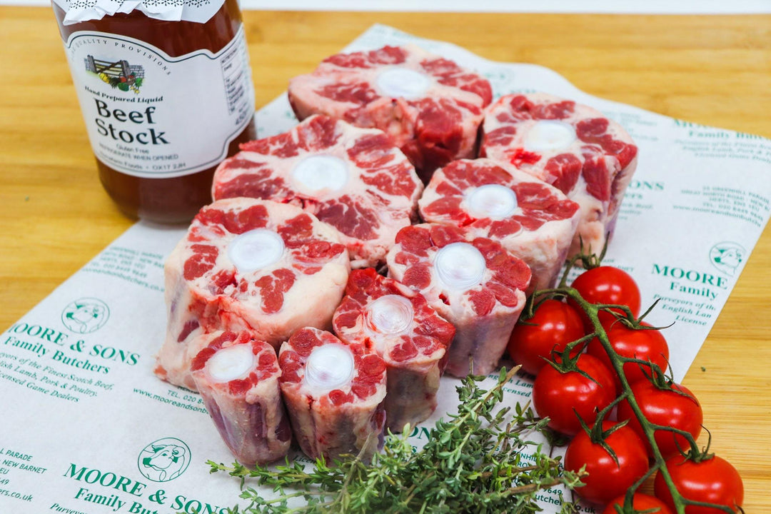 oxtail on a butcher block with tomatoes, herbs and beef stock on the side