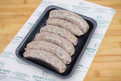 six pork and leek sausages on a black tray on top of a butchers block