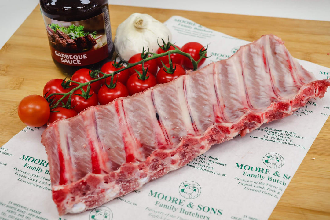 pork rack baby back rib on a butchers block with tomatoes, garlic and barbeque sauce on the side