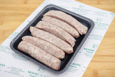 six pork and garlic sausages on a black tray on top of a butchers block