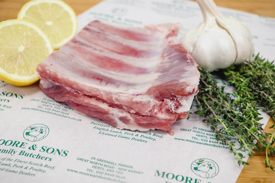pork spare ribs on a butchers block with herbs, garlic and lemons on the side
