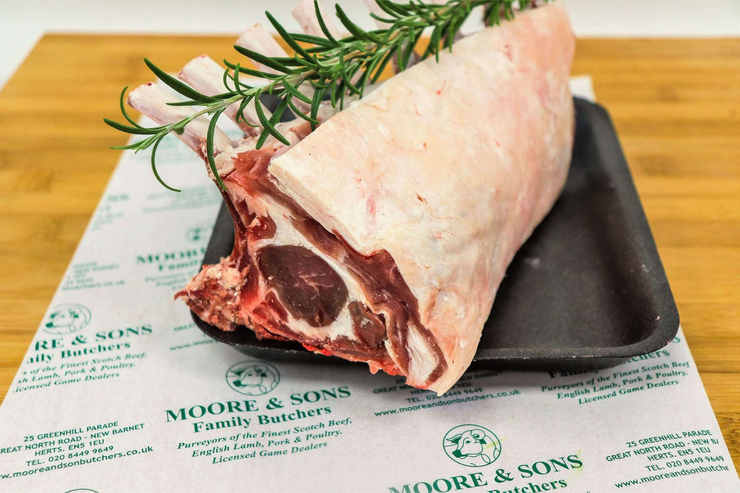 rack of lamb on a butchers block with herbs on the side
