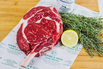 Rib Roast Cote de Beouf on a butcher block with lemon and herbs on the side