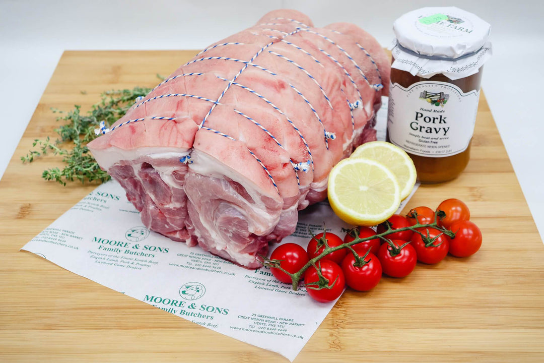 pork shoulder boneless rolled on a butchers block with tomatoes, herbs, lemon and pork gravy on the side
