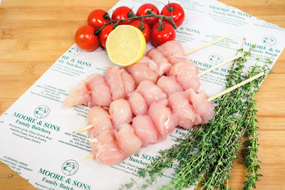 chicken skewers on a butcher block with tomatoes, lemon and herbs on the side