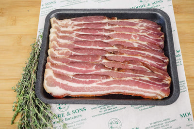 slices of streaky back bacon on a tray, with herbs on the side