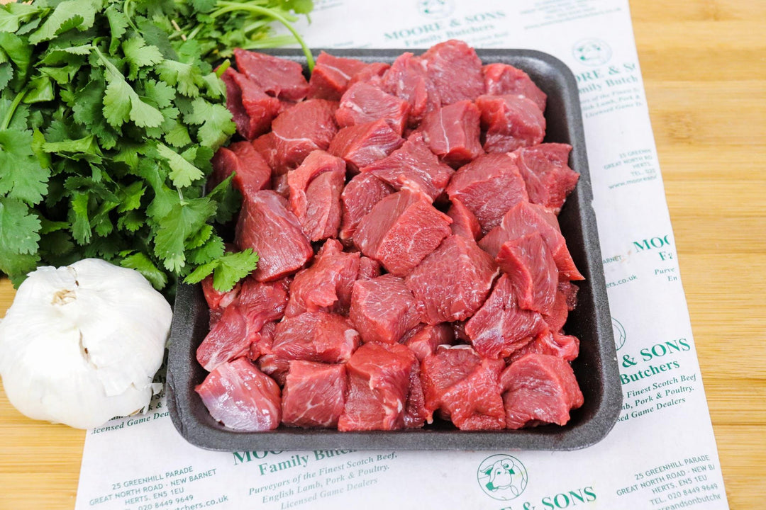 Diced steak on a butcher block with herbs and garlic on the side