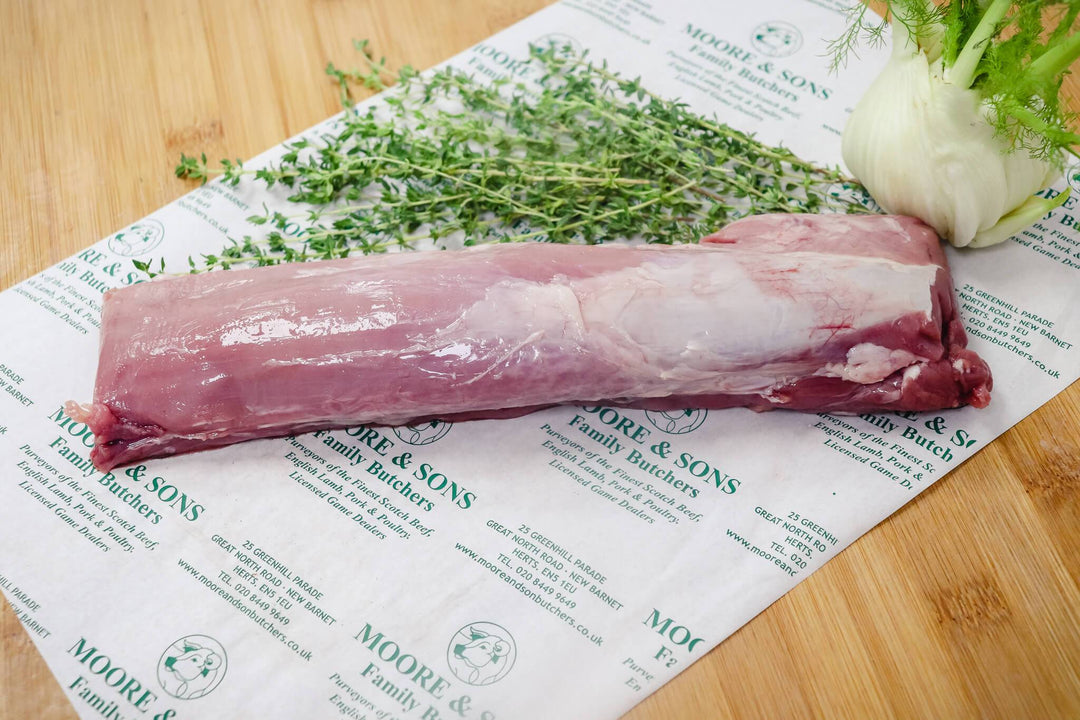 pork tenderloin on a butchers block with green onion and herbs on the side