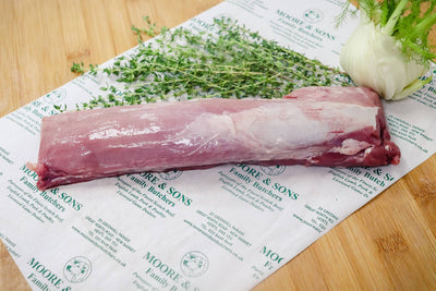 pork tenderloin on a butchers block with green onion and herbs on the side