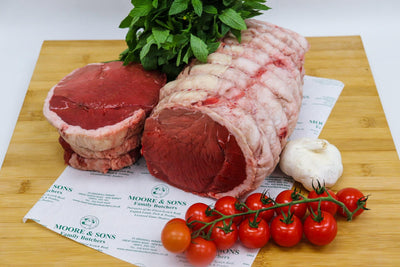 topside joint on a butcher block with tomatoes, garlic and herbs on the side