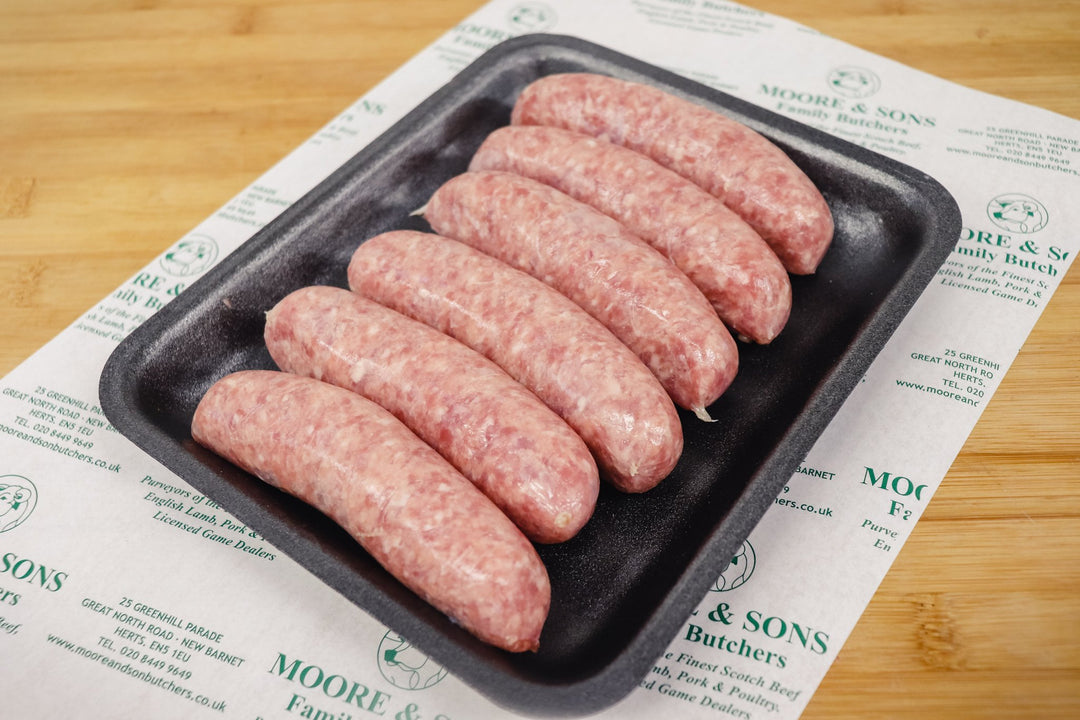 six traditional sausages on a black tray on top of a butchers block