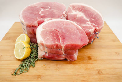 Pieces of unsmoked gammon joint on a butchers block with lemons and herbs on the side