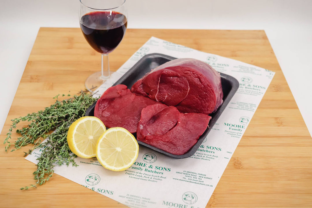 venison steak on a butchers block with lemon, herbs and a glass of wine on the side
